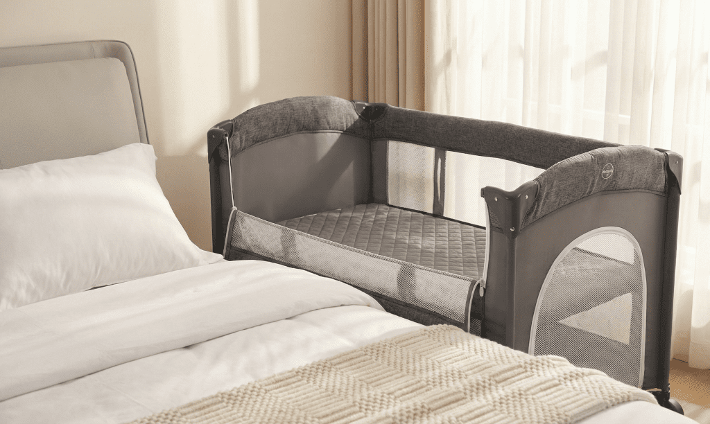 Adovel Bedside Sleeper set up next to an adult bed showing the drop-down side and breathable mesh walls for our Adovel bedside Bassinet Review.