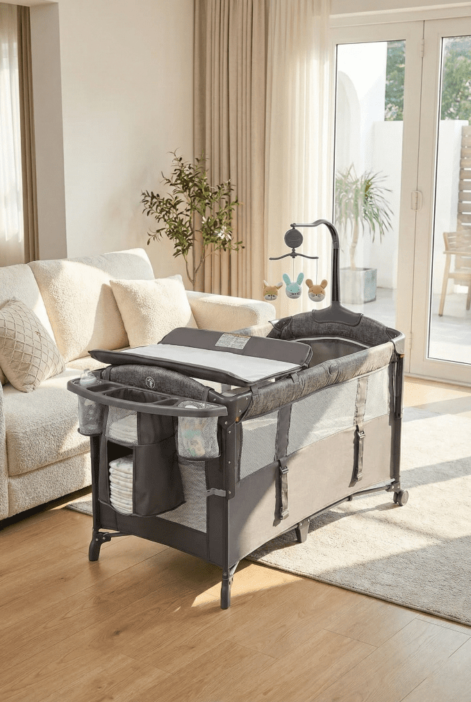 The grey Adovel bassinet on wheels positioned in a sunlit living room next to a couch for daytime naps.