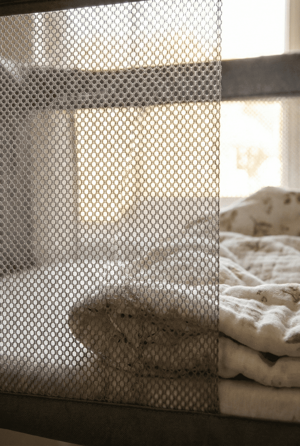Close-up detail of light shining through the grey breathable mesh side walls of the Ingenuity Dream & Grow Bassinet.