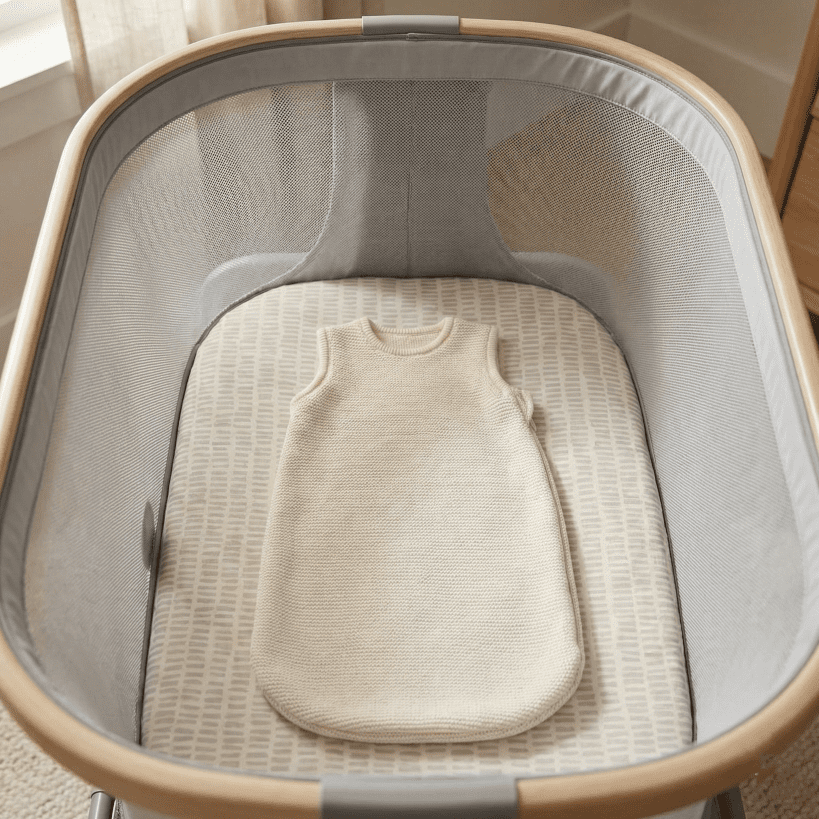 A top-down view inside the Maxi Cosi Iora bassinet, showing the thick mattress, a cozy sleep sack, and the fully breathable mesh walls for safe sleep.