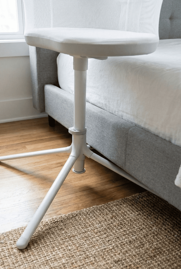 Halo BassiNest 3.0 Review: A C-Section Lifesaver? 3 A photo showing the heavy metal base legs of the Halo BassiNest swivel sleeper sliding underneath an adult bed frame, illustrating the required floor clearance and small footprint.