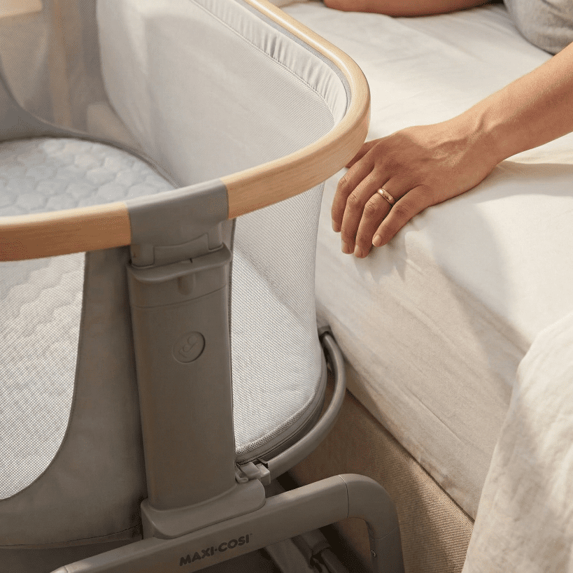 A close-up view of the Maxi Cosi Iora bassinet slid completely against an adult mattress, demonstrating the safe bedside sleeper function without a gap.